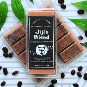 May include: A clear plastic package containing a brown soy wax melt with a black label that reads "Krafty Kitty Studios, The Coffeehouse Collection, Jiji's Blend, Roasted Mocha Java Coffee Beans, Scented Soy Wax Melts, Made in Florida, Hand Poured in Small Batches, Net wt. 2 oz/57 g".