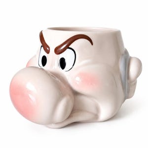 Könnte beinhalten: Ein Keramikbecher in Form eines Cartoon-Charakterkopfes mit einer großen, abgerundeten rosa Nase, markanten braunen Augenbrauen und weit geöffneten Augen. Der Becher hat eine cremefarbene Oberfläche mit zartem rosa Rouge auf den Wangen.