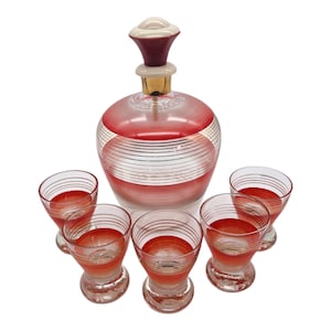 Könnte beinhalten: Vintage Glas-Dekanter-Set mit Dekanter und sechs Gläsern. Der Dekanter hat ein rot-weiß gestreiftes Design mit passendem Verschluss. Die Gläser haben ein ähnliches rot-weißes Design.