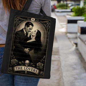Tarot-inspired “The Lovers” tote bag capturing the passionate Morticia and Gomez Addams dynamic. A must-have gothic gift for Addams Family fans, dark romance readers, and vintage art collectors. Handmade by House of Lotus Co on premium black canvas, this mystical tote blends gothic beauty, classic love symbolism, and art deco tarot design.