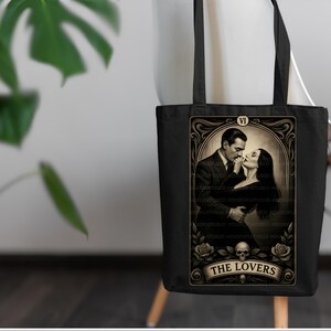 Elegant black tote bag with “The Lovers” tarot artwork inspired by Morticia and Gomez Addams. A perfect handmade Halloween gift for fans of gothic romance, witchy style, and timeless love. Designed by House of Lotus Co, this durable cotton tote embodies dark elegance and tarot symbolism with vintage gold detailing and romantic Addams Family aesthetic.