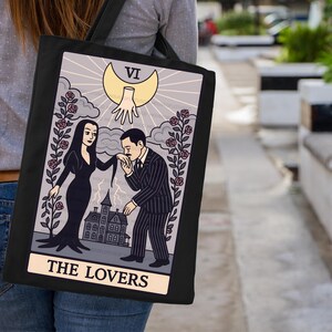 Hand-pressed tote bag featuring Addams Family-inspired tarot design The Lovers. Gothic romantic art with roses, mansion, and crescent moon. Great Halloween tote for witchy fashion lovers.