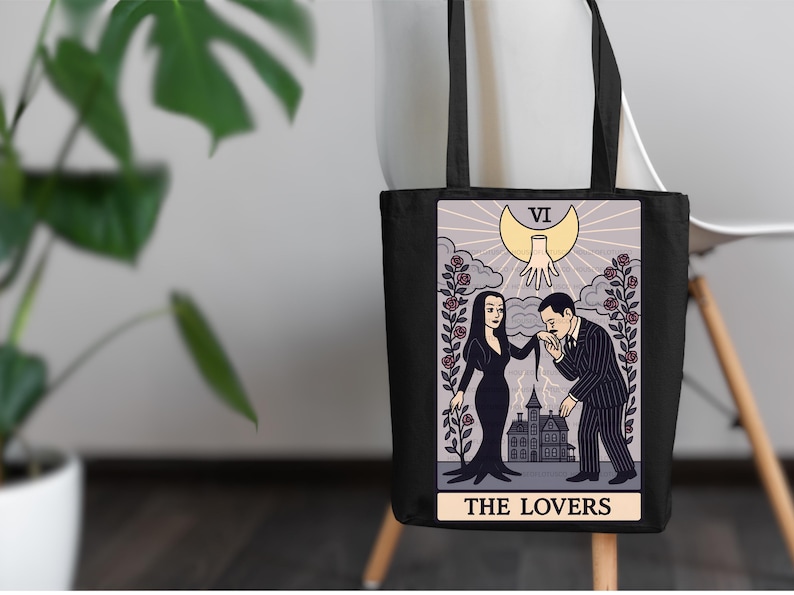 Addams Family tarot tote bag featuring Morticia & Gomez as The Lovers. Gothic artwork with roses, crescent moon, and haunted mansion. Perfect for tarot collectors and witchy Halloween fans.