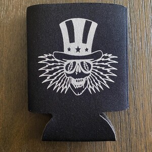 May include: Black neoprene can cooler with a white graphic of a skull wearing a top hat with stars and stripes.