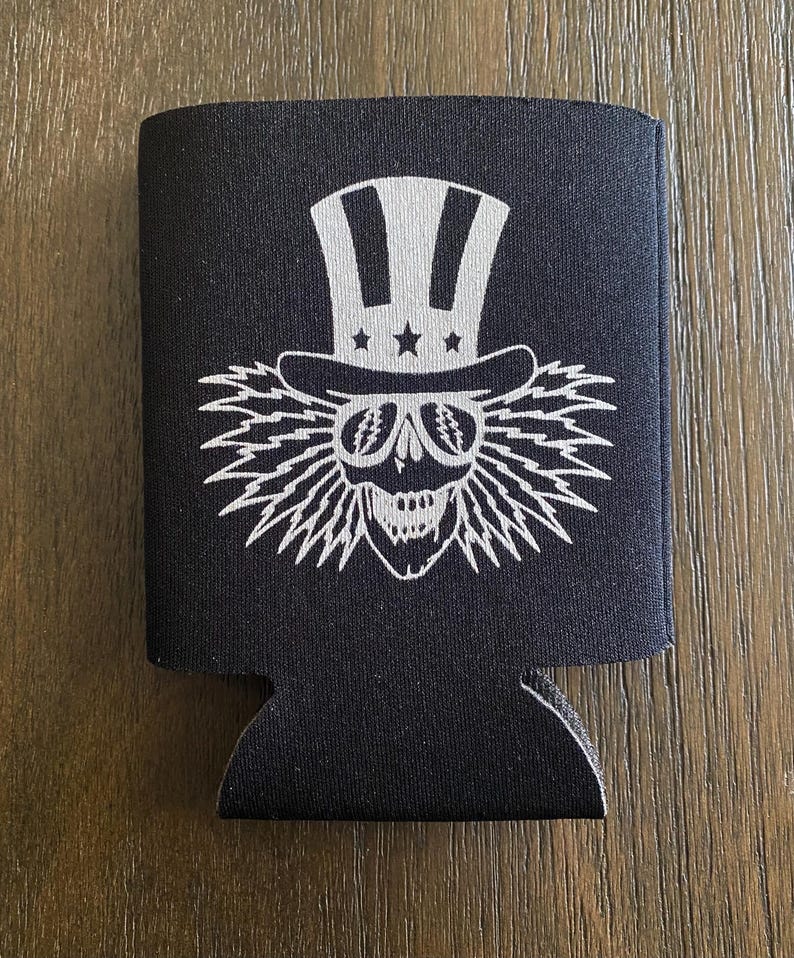 May include: Black neoprene can cooler with a white graphic of a skull wearing a top hat with stars and stripes.