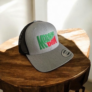 May include: A grey and black trucker hat with a green and red "MORNING DEW" logo embroidered on the front.