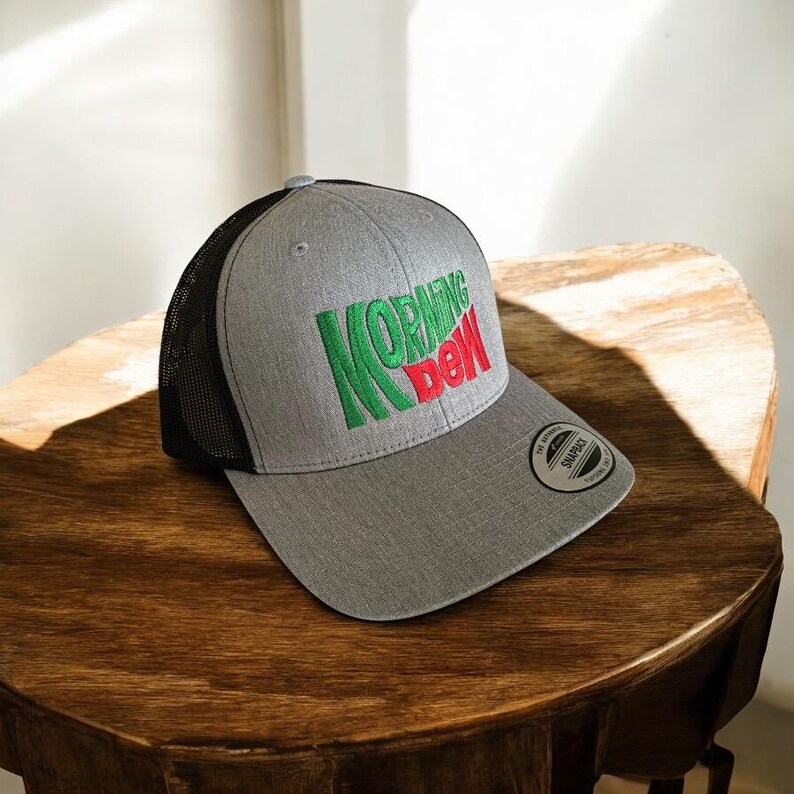 May include: A grey and black trucker hat with a green and red "MORNING DEW" logo embroidered on the front.