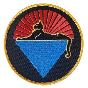 Puede incluir: Parche bordado circular con la silueta de un gato negro sobre un triángulo azul, sobre un diseño de rayos de sol rojos. El parche tiene un fondo azul marino y un borde dorado.