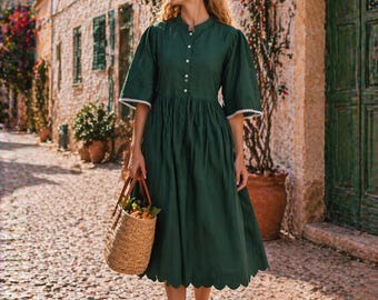 May include: A woman wearing a dark green dress with a scalloped hem and white trim on the sleeves. She carries a woven basket with fruit. The dress has a button-down front and a high neckline. She is walking on a cobblestone street.