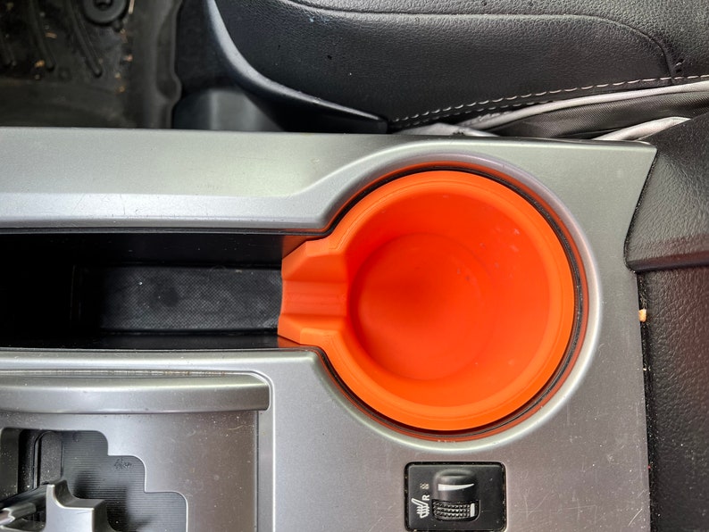May include: A close-up of a car's center console with a gray and black interior. The console features a cup holder with an orange silicone insert.