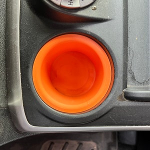 May include: A close-up of an orange cup holder in a car. The cup holder is made of a soft, flexible material and is designed to fit standard-sized cups.
