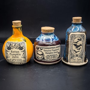 Puede incluir: Tres botellas de poción de cerámica con tapones de corcho. Las botellas son naranjas, azules y marrones, con etiquetas que dicen "Rotten Pumpkin Juice", "Genuine Powdered Vampire Fangs" y "Bat Eyes". Las botellas son para Halloween.