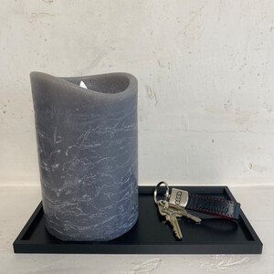 Könnte beinhalten: Ein schwarzes Tablett mit einer grauen Kerze und einem Schlüsselsatz mit einem Audi-Schlüsselanhänger. Der Schlüsselanhänger hat ein rotes Lederband mit dem geprägten Wort "Audi".