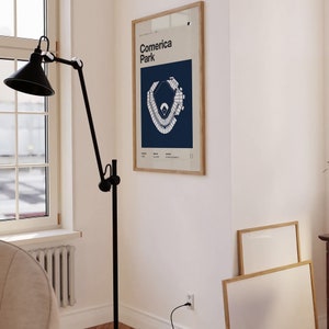 May include: A framed print of a baseball field map with the text "Comerica Park" in a white sans-serif font on a blue background. The print is hanging on a white wall.
