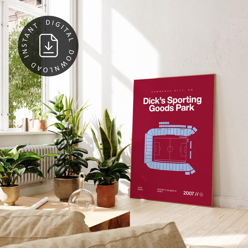 May include: A burgundy poster featuring a light blue stadium layout with the text "Dick's Sporting Goods Park" in white. The poster includes the location and year 2007. The image is in a well-lit room with plants.