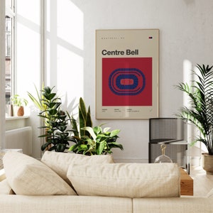 K&ouml;nnte beinhalten: Ein gerahmtes Poster mit dem Text "Centre Bell" und einer Stadiongrafik in Rot und Blau. Das Poster wird an einer wei&szlig;en Wand ausgestellt, umgeben von Pflanzen und einem Sofa.