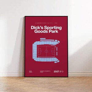 May include: A framed poster with a burgundy background features a light blue stadium layout. The text "Dick's Sporting Goods Park" is in white. Additional text includes "COMMERCE CITY, CO", "18,061 Capacity", "39.8056 N 104.8918 W Location", and "2007 //".