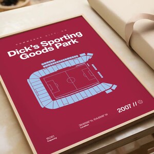 May include: Framed print of Dick's Sporting Goods Park in Commerce City, CO. The stadium is depicted in a light blue schematic on a maroon background. Text includes the stadium name, location coordinates, capacity, and the year 2007.