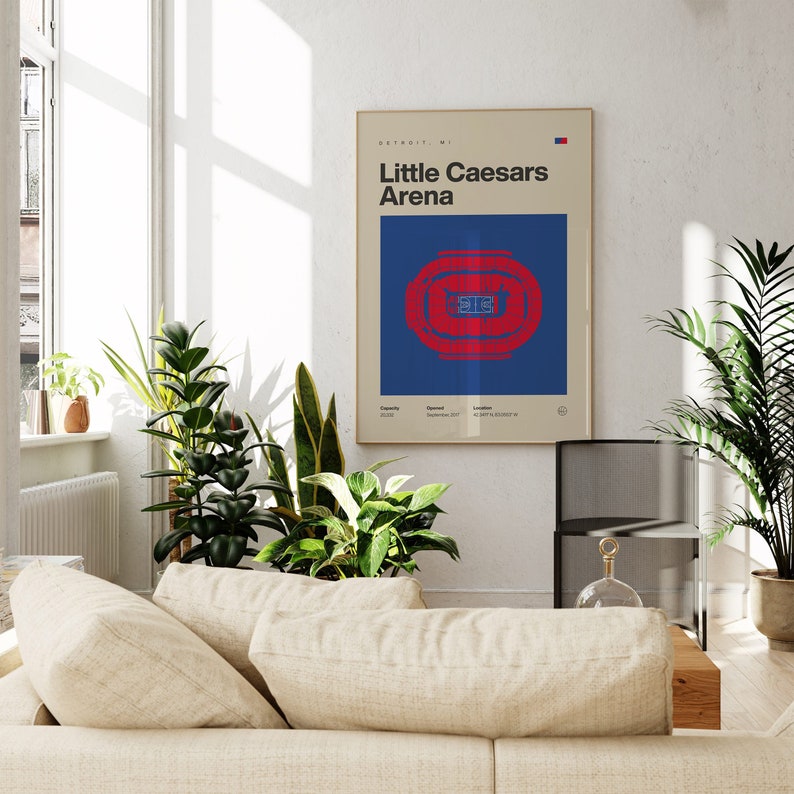 以下が含まれることがあります： デトロイトのLittle Caesars Arenaのミニマルなグラフィックが描かれた額入りウォールポスター。デザインには「Little Caesars Arena」の文字、青い背景に赤いスタジアムの座席図、収容人数と場所のデータが含まれています。