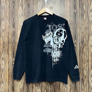 May include: Black long-sleeve shirt with a graphic design on the front. The design includes the words "Another State of Mind" and a stylized face. The shirt is hanging on a wooden hanger against a wood-paneled background.