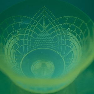 May include: A clear glass bowl with an intricate, geometric design etched into its surface. The bowl has a wide, shallow shape with a circular base and a detailed pattern that resembles a stylized flower or architectural element. The color is a gradient of green.