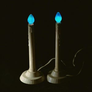 Pode incluir: Duas lâmpadas elétricas em forma de vela de cor marfim com lâmpadas azuis brilhantes. As lâmpadas têm um design clássico com uma base, um caule alto e um efeito de cera pingando. As lâmpadas estão ligadas e prontas para uso.