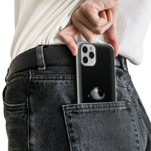 May include: A black phone case with a white eye design is tucked into the back pocket of a pair of dark gray jeans.