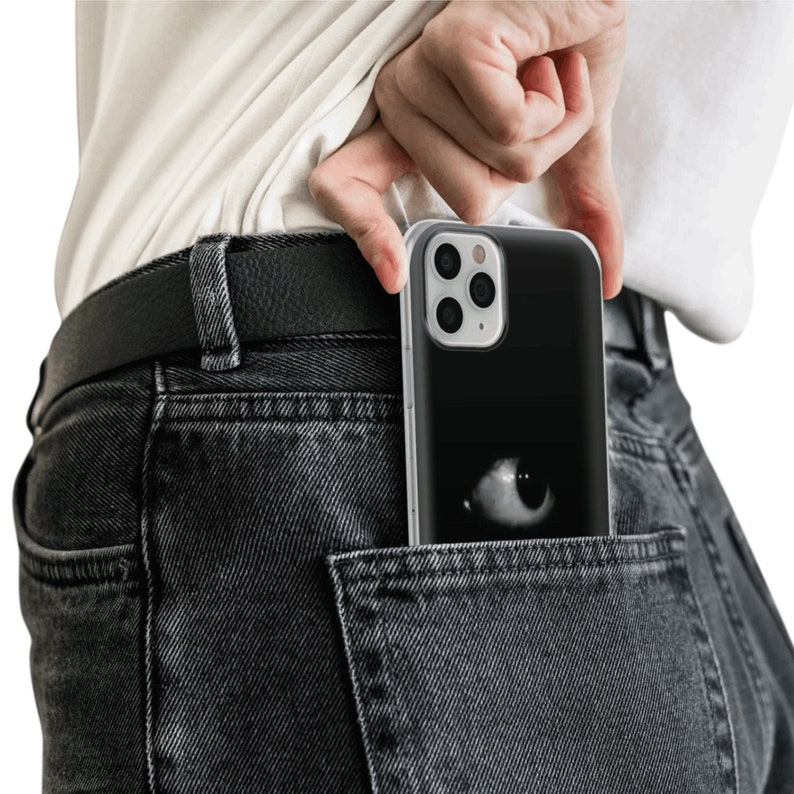 May include: A black phone case with a white eye design is tucked into the back pocket of a pair of dark gray jeans.