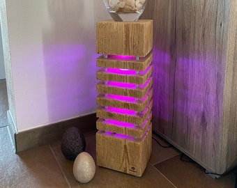 Puede incluir: Una lámpara de madera con luz morada, con un diseño apilado de múltiples capas. La lámpara está sobre una base de madera y tiene un jarrón de vidrio con una planta en la parte superior. La lámpara está iluminada con luz morada.