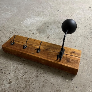 Könnte beinhalten: Ein Holz-Kleiderständer mit fünf Haken und einer schwarzen Metallkugel an einem Schwenkarm. Der Ständer ist aus recyceltem Holz gefertigt und hat einen rustikalen Look.