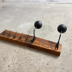 Könnte beinhalten: Ein Holz-Kleiderständer mit acht Haken und zwei schwarzen Metallkugeln. Der Ständer ist aus recyceltem Holz gefertigt und hat eine rustikale Oberfläche.