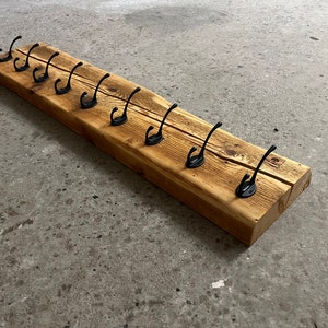 Könnte beinhalten: Ein rustikaler Holz-Kleiderständer mit 10 schwarzen Metallhaken. Der Ständer ist aus recyceltem Holz gefertigt und hat eine natürliche, gewitterte Oberfläche.