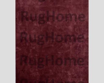 May include: A burgundy rug with the text "RugHome" repeated vertically. The rug has a textured appearance, and the lettering is a darker shade of burgundy.