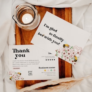 Puede incluir: Una tarjeta de agradecimiento con un diseño de abeja y flores. La tarjeta dice "Gracias" y "¡Espero que disfrutes de tu pedido tanto como yo disfruté creándolo! Para mostrarte mi agradecimiento, aquí tienes un 10% de descuento en tu próximo pedido con el código: THANKS10". La tarjeta también tiene un espacio para un logotipo y la información de contacto.