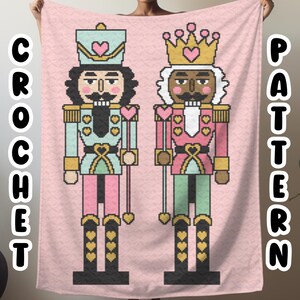 May include: A pink crochet blanket with a pixelated design of two nutcracker figures. The nutcracker on the left is wearing a blue and pink uniform and a crown. The nutcracker on the right is wearing a pink and green uniform and a crown. The blanket has the words "CROCHET PATTERN" on the left and right sides.