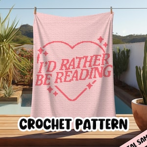 Könnte beinhalten: Ein rosa Häkeldeckenmuster mit einem herzförmigen Design, auf dem "Ich würde lieber lesen" steht.