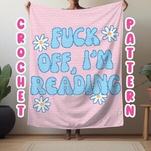 Puede incluir: Manta de crochet rosa con el texto "F*CK OFF, I'M READING" en letras pixeladas azules y flores de margarita blancas.