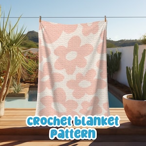 Puede incluir: Una manta de ganchillo con un patrón repetido de grandes flores de color rosa claro sobre un fondo crema. La manta está colgada en un tendedero al aire libre. El texto "CROCHET blanket Pattern" se muestra en la parte inferior.