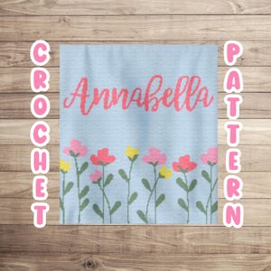 May include: A crochet pattern for a baby blanket with a blue background, pink flowers, and the name "Annabella" in pink lettering.