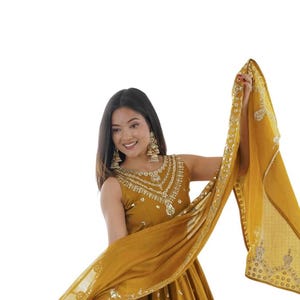 May include: A mustard yellow sleeveless floor-length dress featuring a round neckline with intricate silver embroidery and small circular mirror embellishments scattered across the skirt, paired with a matching sheer dupatta with silver border.