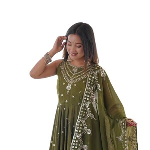 Puede incluir: Un vestido largo sin mangas de color verde oliva con intrincados bordados plateados y detalles de espejos en el escote y el corpiño. El vestido incluye una dupatta a juego de tela transparente con un borde decorativo bordado en plata.