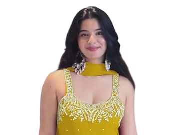 May include: A mustard yellow sleeveless kurta and sharara set featuring white beaded embroidery along the neckline and hem. The garment is adorned with scattered white pearl-like embellishments throughout the fabric and includes a matching scarf.