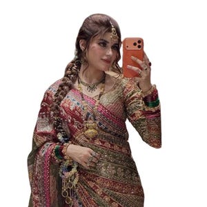 Peut inclure: Un sari à manches longues présentant une palette de couleurs rouge profond et vert olive avec des broderies dorées complexes et des détails à paillettes. Le vêtement comprend un chemisier assorti, un pallu drapé et des bijoux superposés.