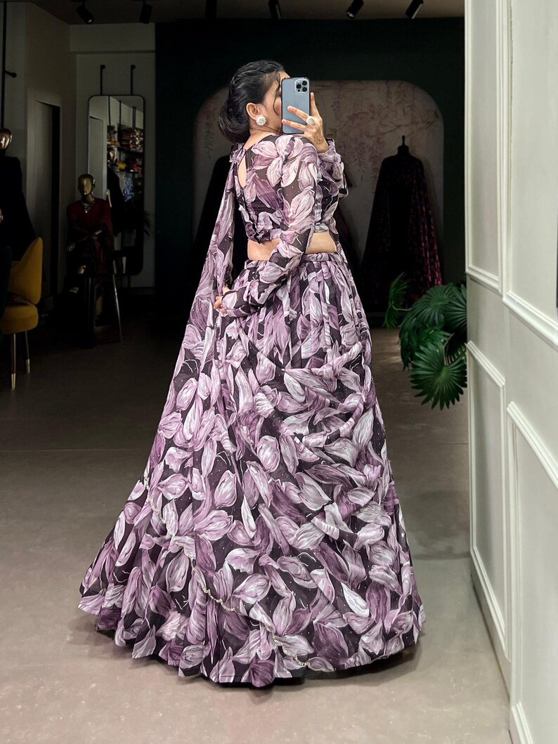May include: A woman wearing a purple and white floral print maxi skirt with a matching crop top. The skirt has a ruffled hem and the top has long sleeves.