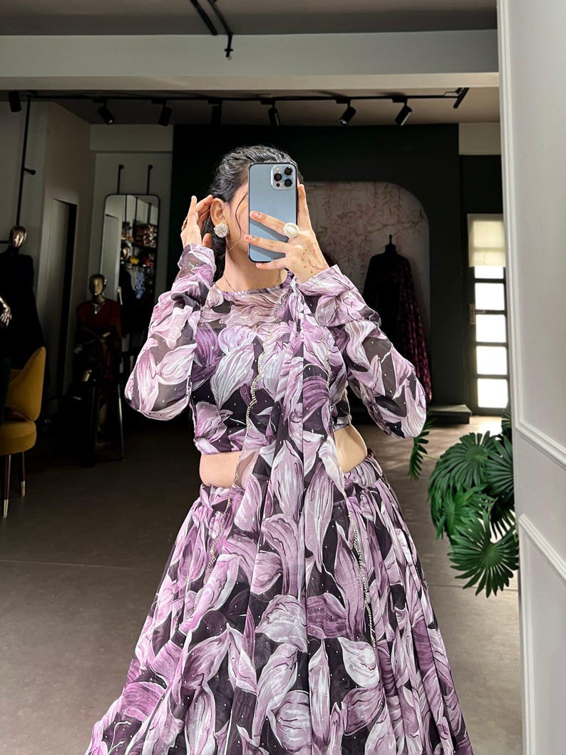 May include: A long-sleeved, purple and white floral print dress with a high neckline and a fitted bodice. The dress has a flowing skirt with a side slit and a silver chain detail.