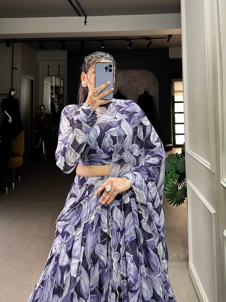 May include: A woman wearing a purple and white floral print dress with a high neck and long sleeves. The dress has a ruffled hem and is made of a sheer fabric.