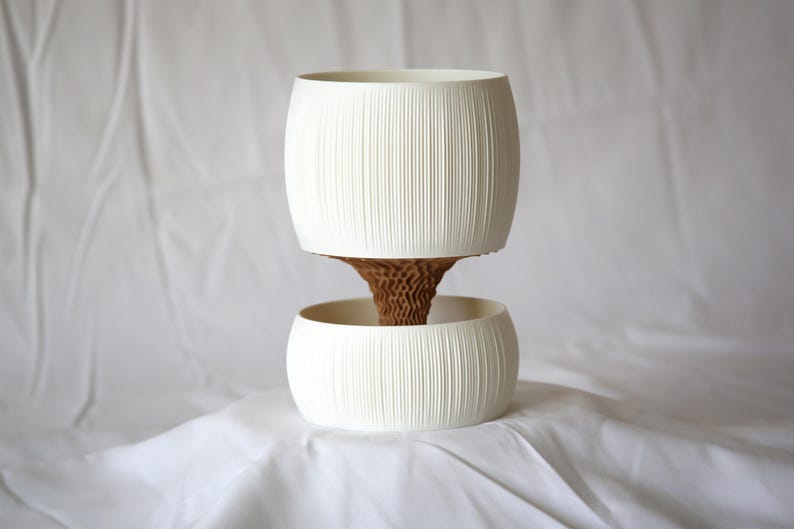 Front view of a cream-white textured matte planter with vertical ribbing, a ribbed pot above a round lower bowl joined by a brown honeycomb-textured core, on white fabric.