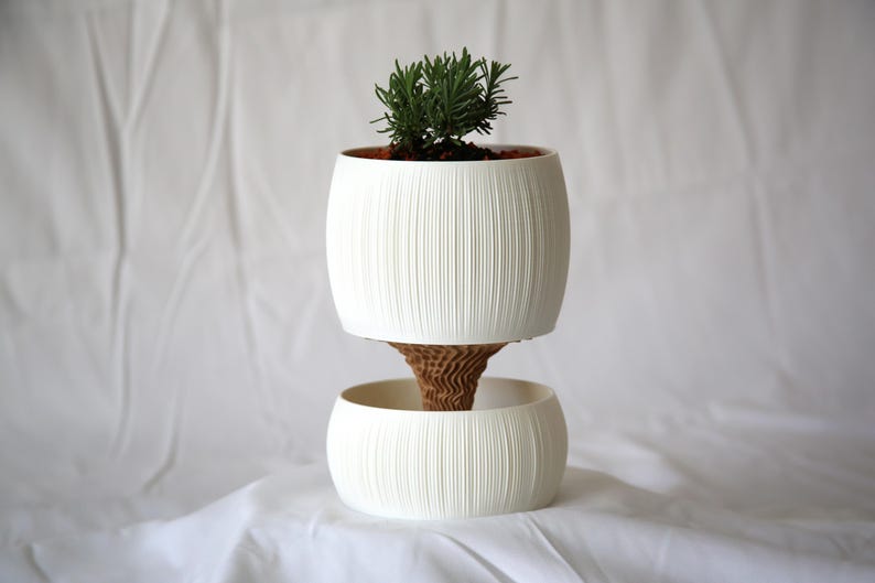 Textured matte white ribbed pot planted with a small green succulent, set over a lower bowl on soft white fabric, a self watering pot with a clean minimal look.