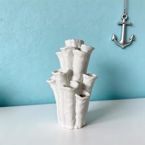 Matte white textured coral vase on a light blue backdrop, with a small anchor charm hanging beside it for a coastal look. Coral vase about 7.2 in tall and 3.9 in wide.