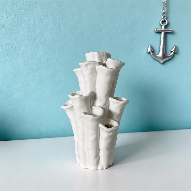 Matte white textured coral vase on a light blue backdrop, with a small anchor charm hanging beside it for a coastal look. Coral vase about 7.2 in tall and 3.9 in wide.